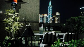An outdoor dining area with a table, chairs, a potted plant, and a table lamp. In the background, a city skyline with illuminated buildings is visible. - Kimpton Da an Taipei by IHG (Taipei)