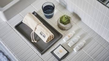 A bathroom with a towel, a glass of water, a small potted plant, and toiletries on a tiled counter.