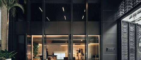 A modern hotel entrance with glass doors, a reception desk, and a seating area.