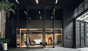 Hall de hotel moderno com portas de vidro, balcão de recepção e área de estar.