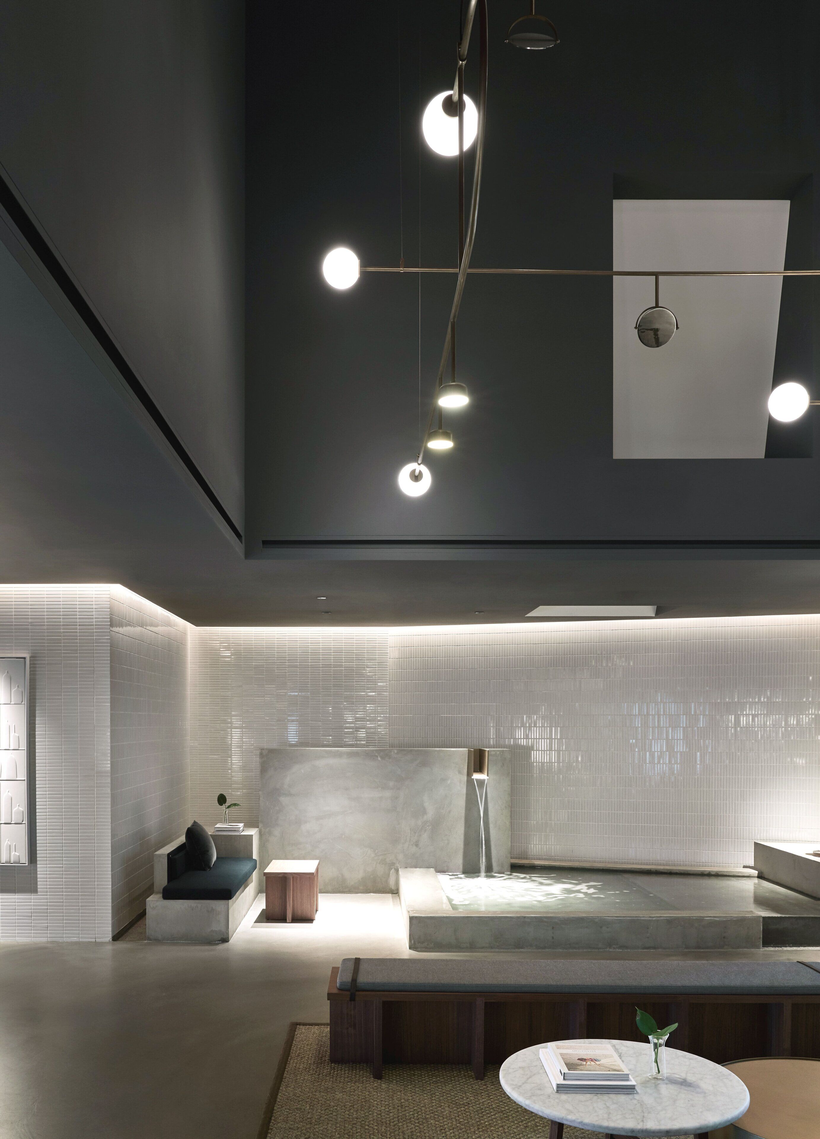 Un interior moderno con diseño minimalista, que incluye una zona de estar, una mesita con un libro y un jarrón, y una lámpara de pared.