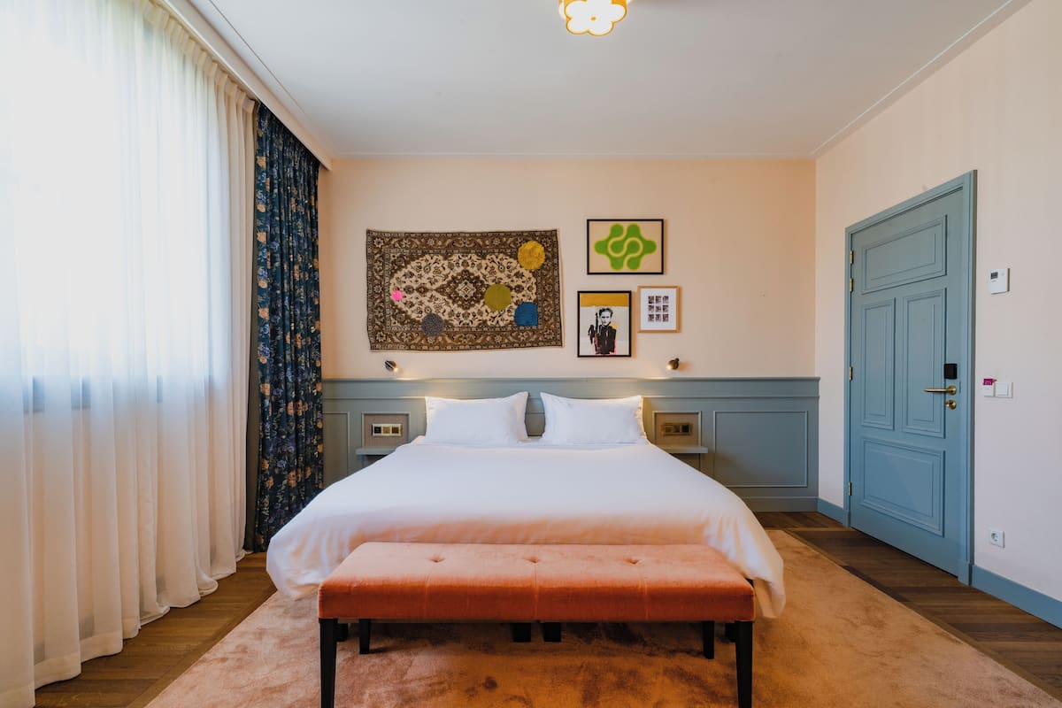 A bedroom with a large bed, a bench, a nightstand, a blue door, and wall art.