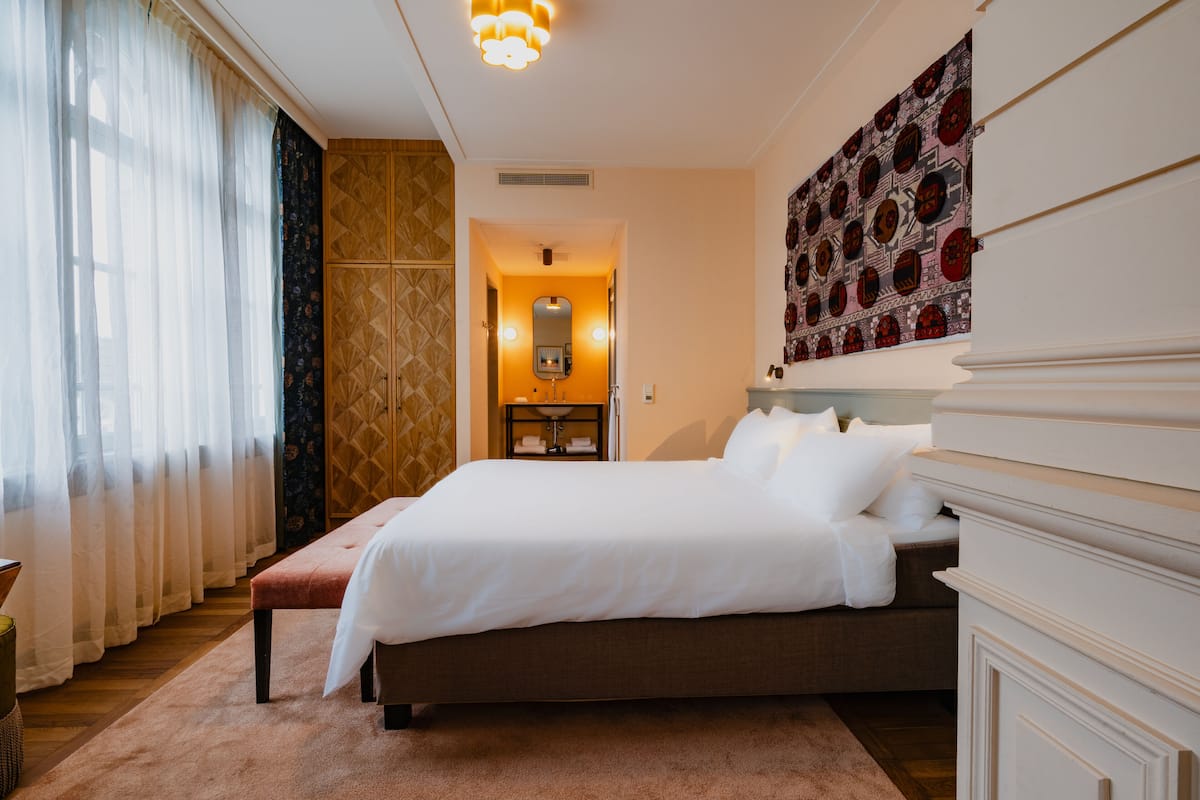 A hotel room with a large bed, a bedside table, a mirror, and a wall with a patterned artwork.