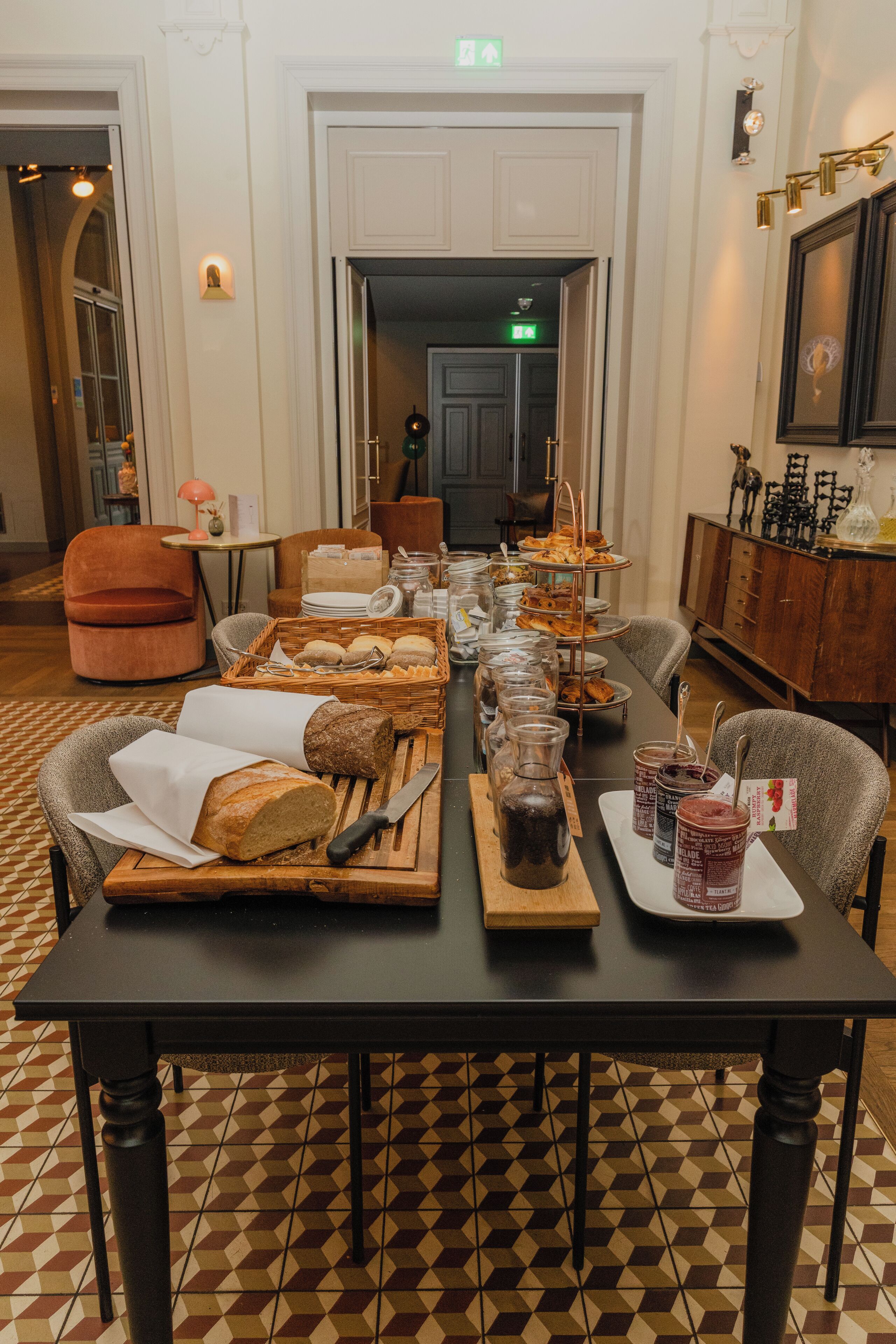A dining table set with bread, jars of preserves, and a knife.
