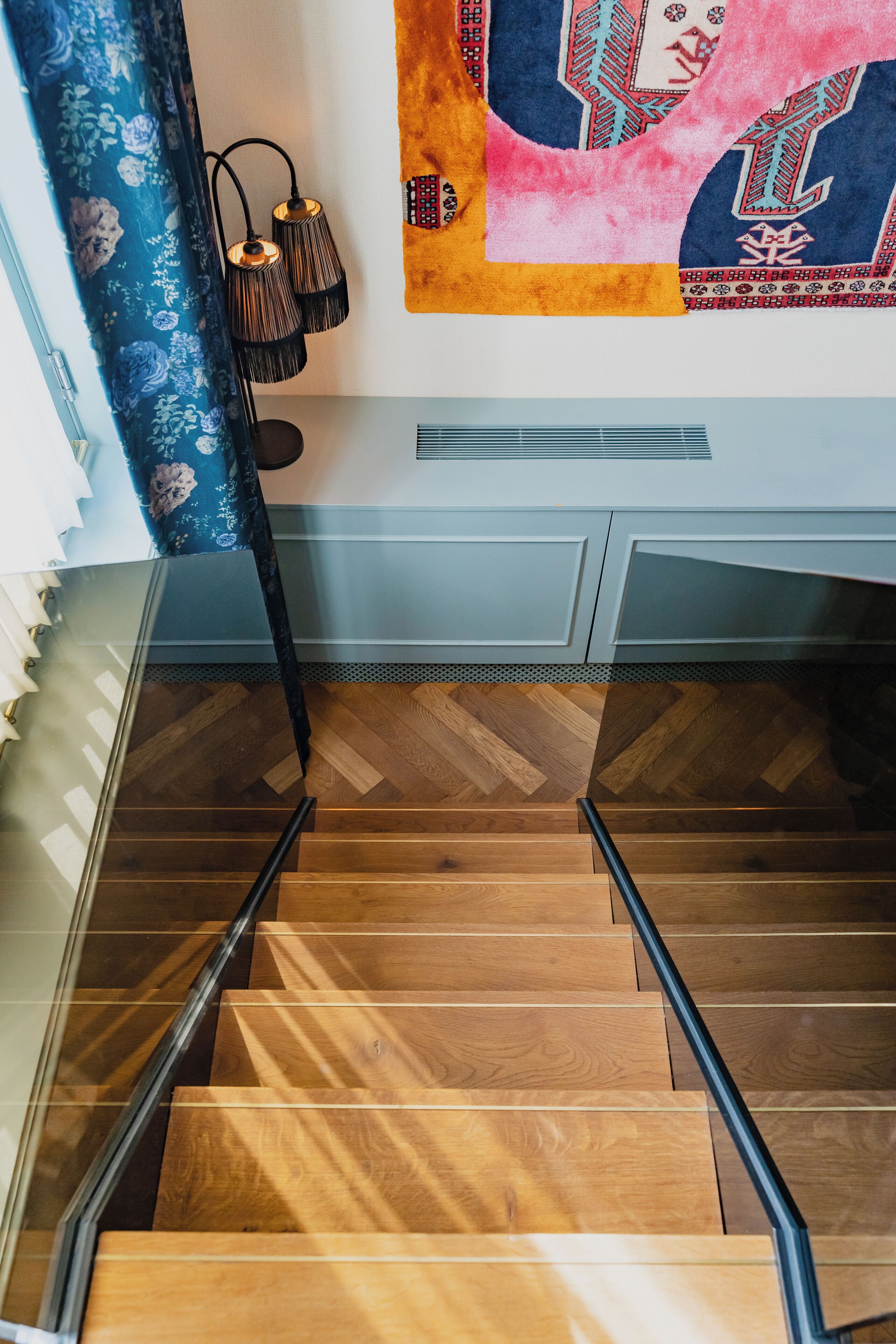Eine Treppe mit Holzdielen und schwarzen Geländern, die zu einem Raum führt, der einen gemusterten Teppich und eine Wandleuchte aufweist.