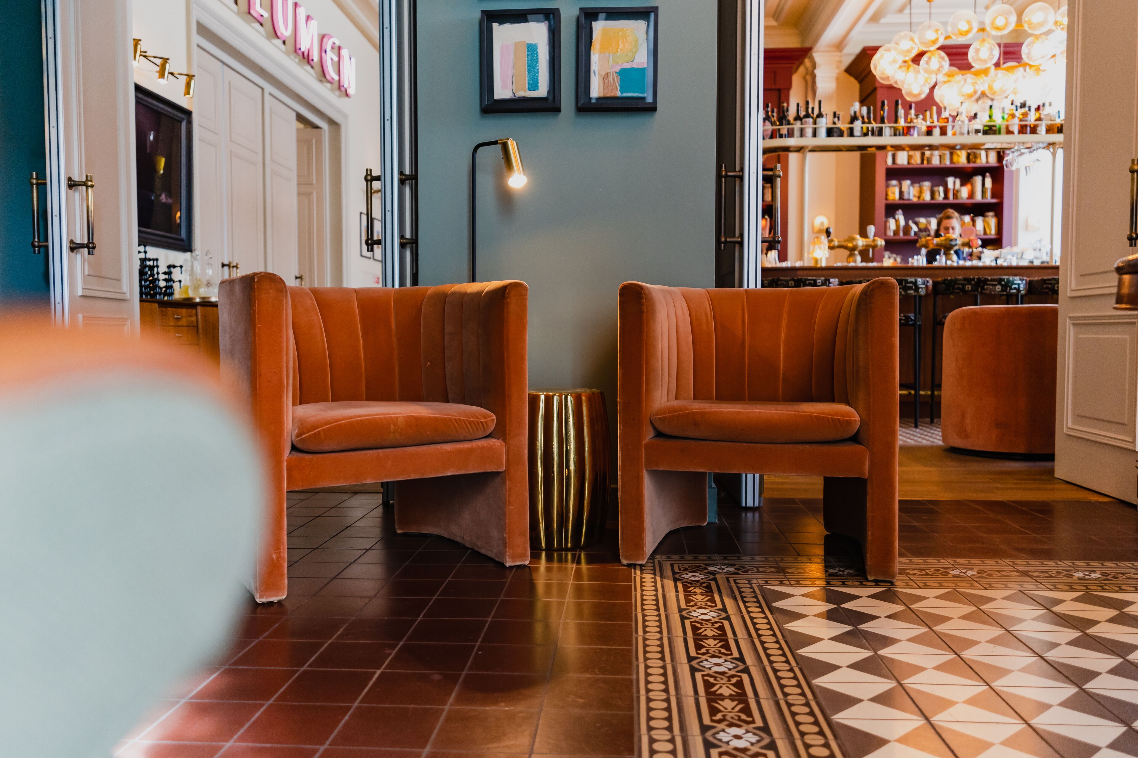 Un coin bar avec deux chaises orange, un sol à motifs et un comptoir bien garni de bouteilles.