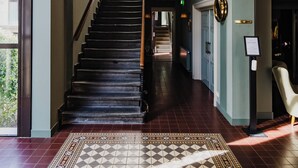 A grand staircase with a patterned rug, a chandelier, and a view of the outdoors. - Hotel Mercier (Amsterdam)