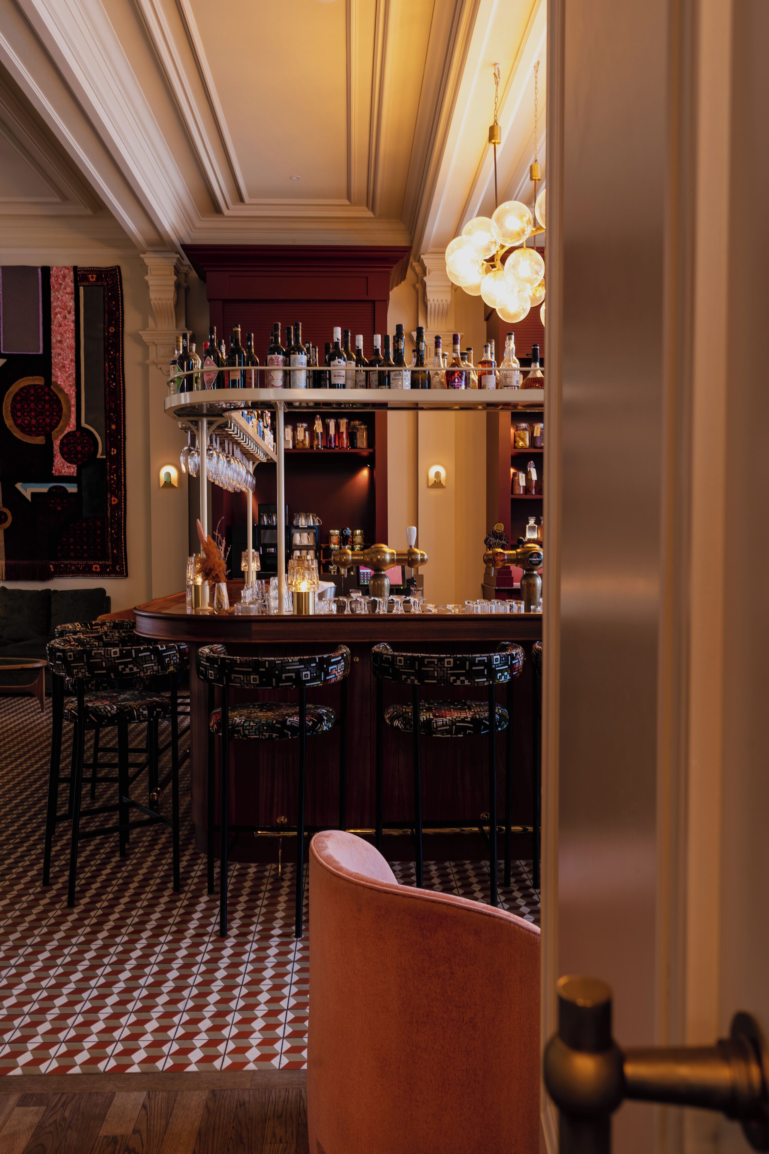 Una zona de bar con suelo a cuadros, taburetes y una estantería para vinos.