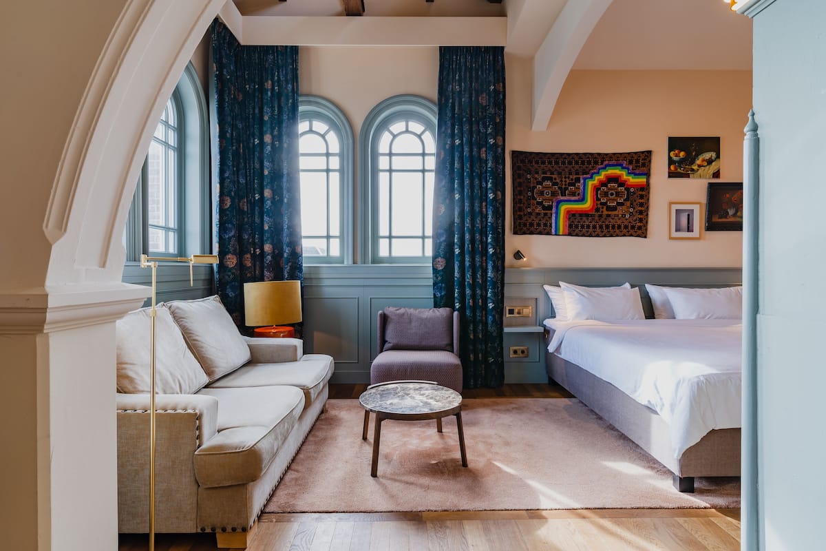A hotel room with a sofa, armchair, round coffee table, and a bed.
