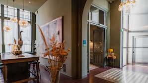 A spacious lobby with a wooden reception desk, a large vase with dried flowers, and a modern chandelier. - Hotel Mercier (Amsterdam)