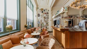 A bar area with a wooden counter, round tables, and cushioned seating. - Hotel Mercier (Amsterdam)