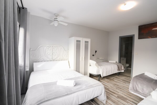 A hotel room with two beds, a wardrobe, a ceiling fan, and a painting on the wall.