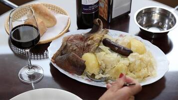 Un plato con carne asada, papas y chucrut, una copa de vino tinto y una botella de vino sobre una mesa.