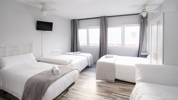 A hotel room with three beds, a flat-screen TV, and a large window with curtains. - Pension Caldas (Caldas de Reis)
