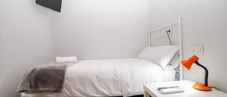 Un dormitorio pequeño y ordenado, con cama, mesita de noche con lámpara y televisión montada en la pared.