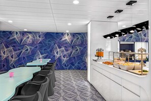 Un espace repas moderne avec un mur décoré de motifs, un buffet proposant divers plats et une disposition des sièges comprenant des tables et des chaises.