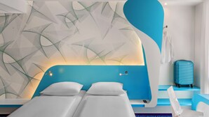 A modern hotel room with a unique wall design, a bed, a suitcase, and a chair.