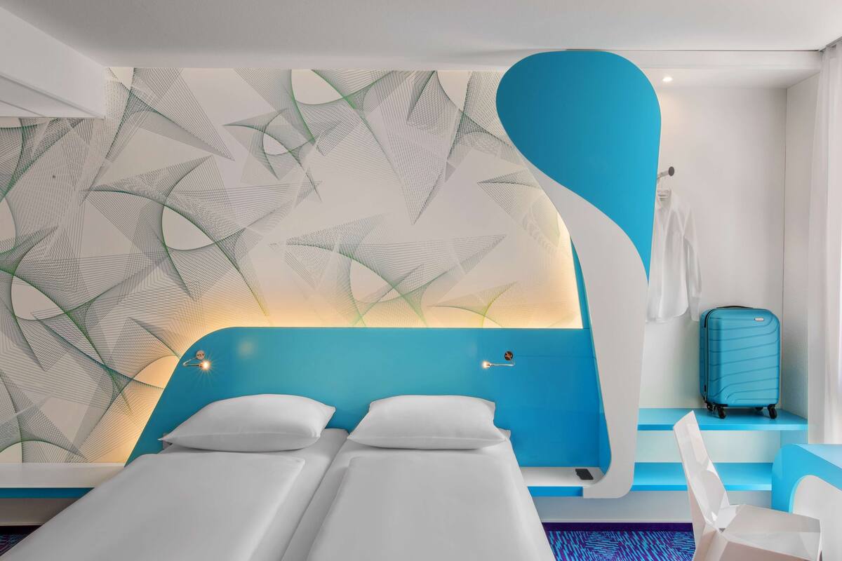 Ein modernes Hotelzimmer mit einem einzigartigen Wanddesign, einem Bett, einem Koffer und einem Sessel.