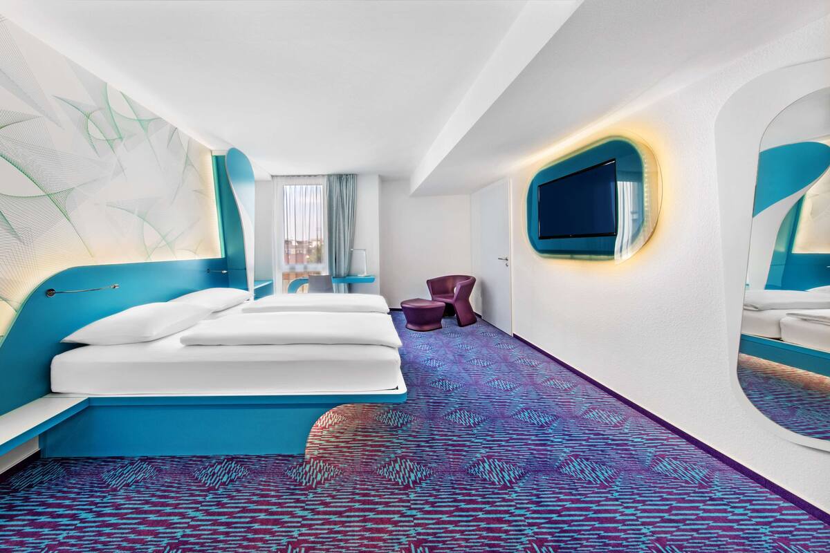 Ein modernes Hotelzimmer mit einem Bett, einem Schreibtisch, einem Stuhl und einem Fernseher.