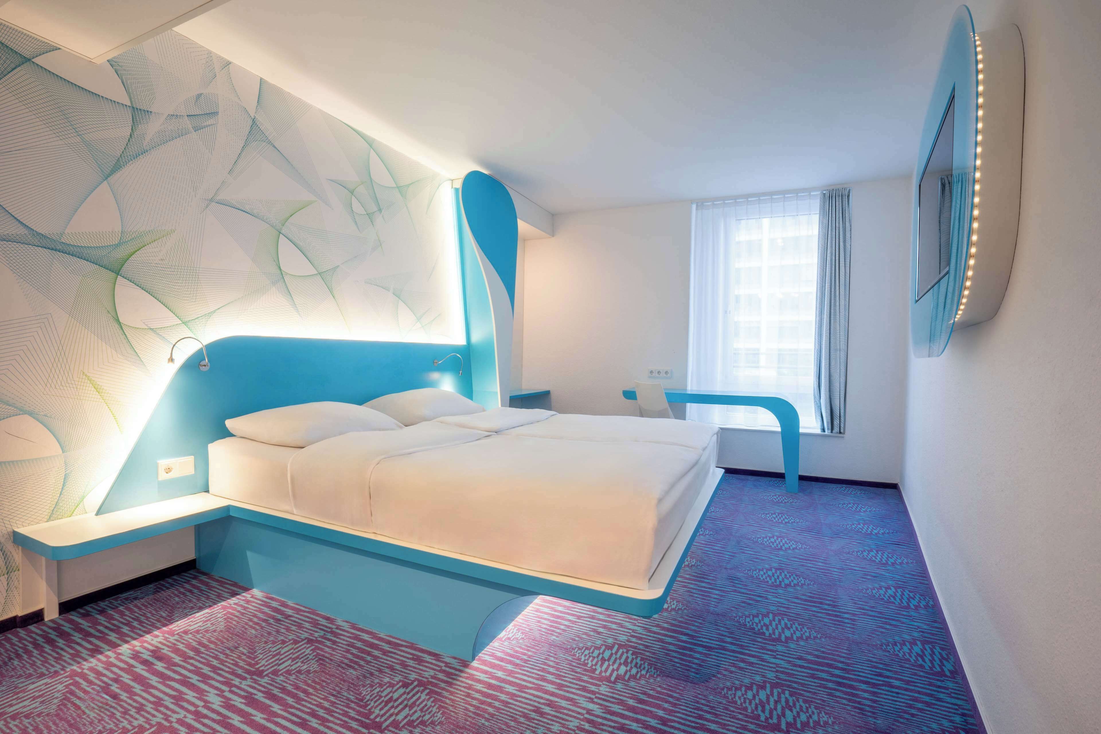 A modern hotel room with a large bed, a desk, and a chair.