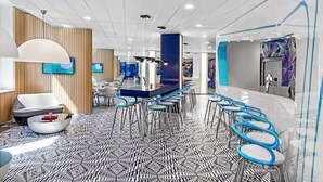 A modern hotel lobby with a long reception desk, blue bar stools, and a patterned floor.
