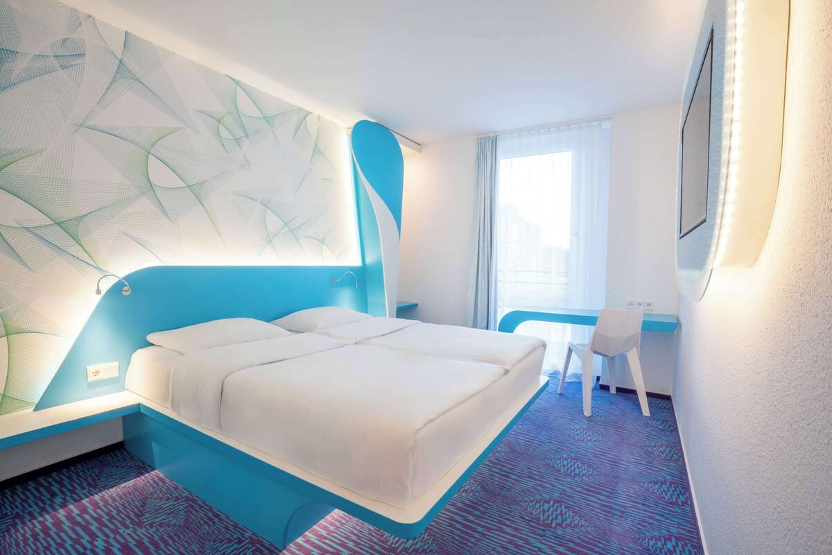 Ein modernes Hotelzimmer mit einem großen Bett, einem Schreibtisch und einem Stuhl.