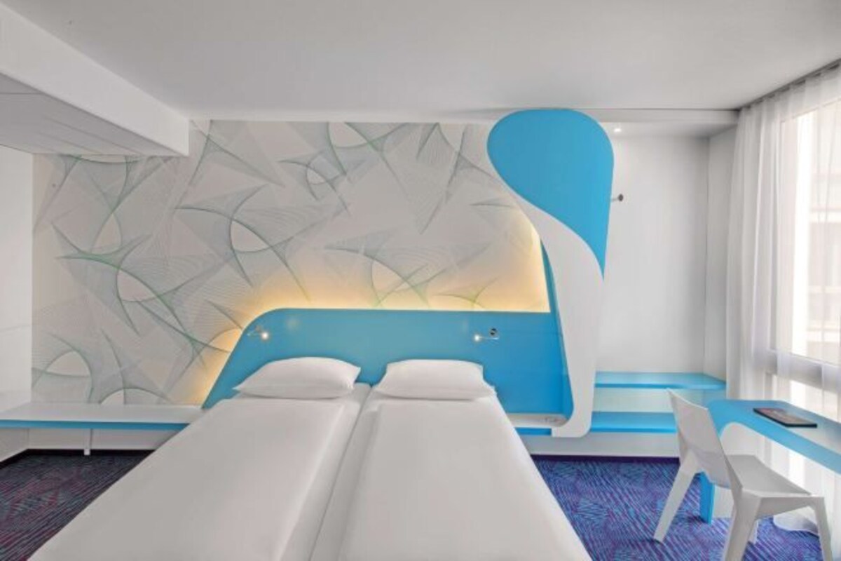 Een kamer met een modern design, met een groot bed in een opvallend blauw-wit kleurenschema, een witte stoel en een behang met een patroon.