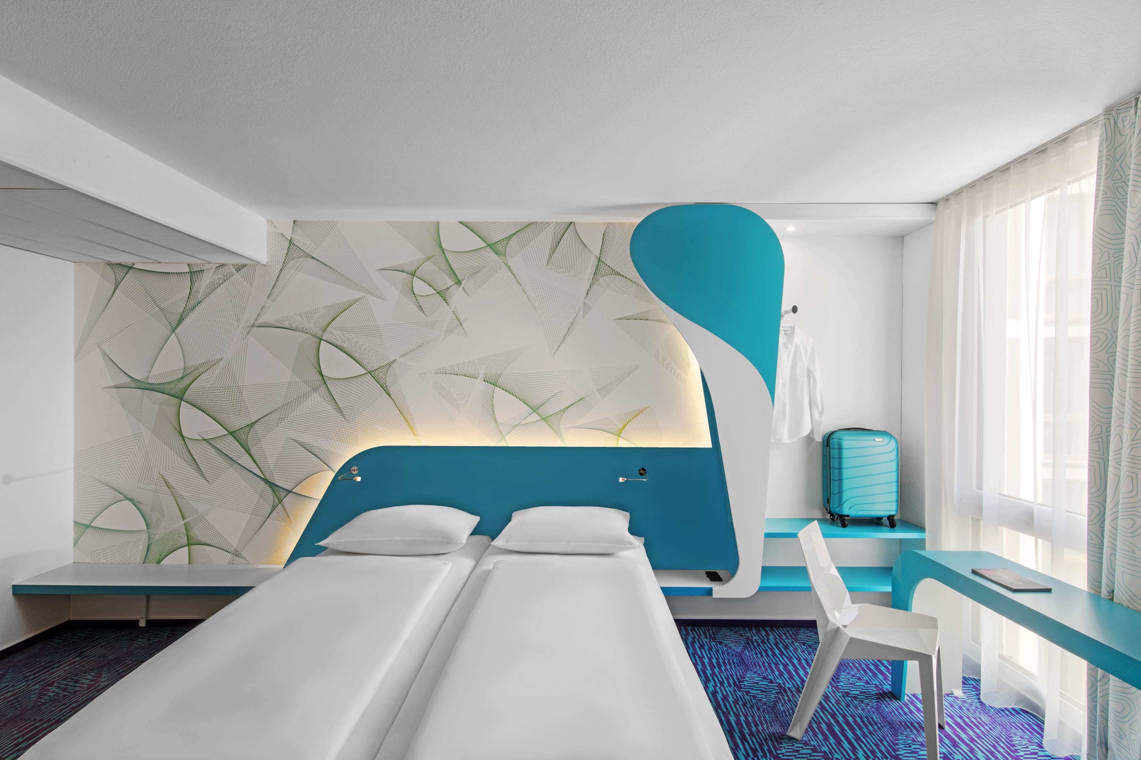 A modern hotel room with two beds, a desk, and a large window.