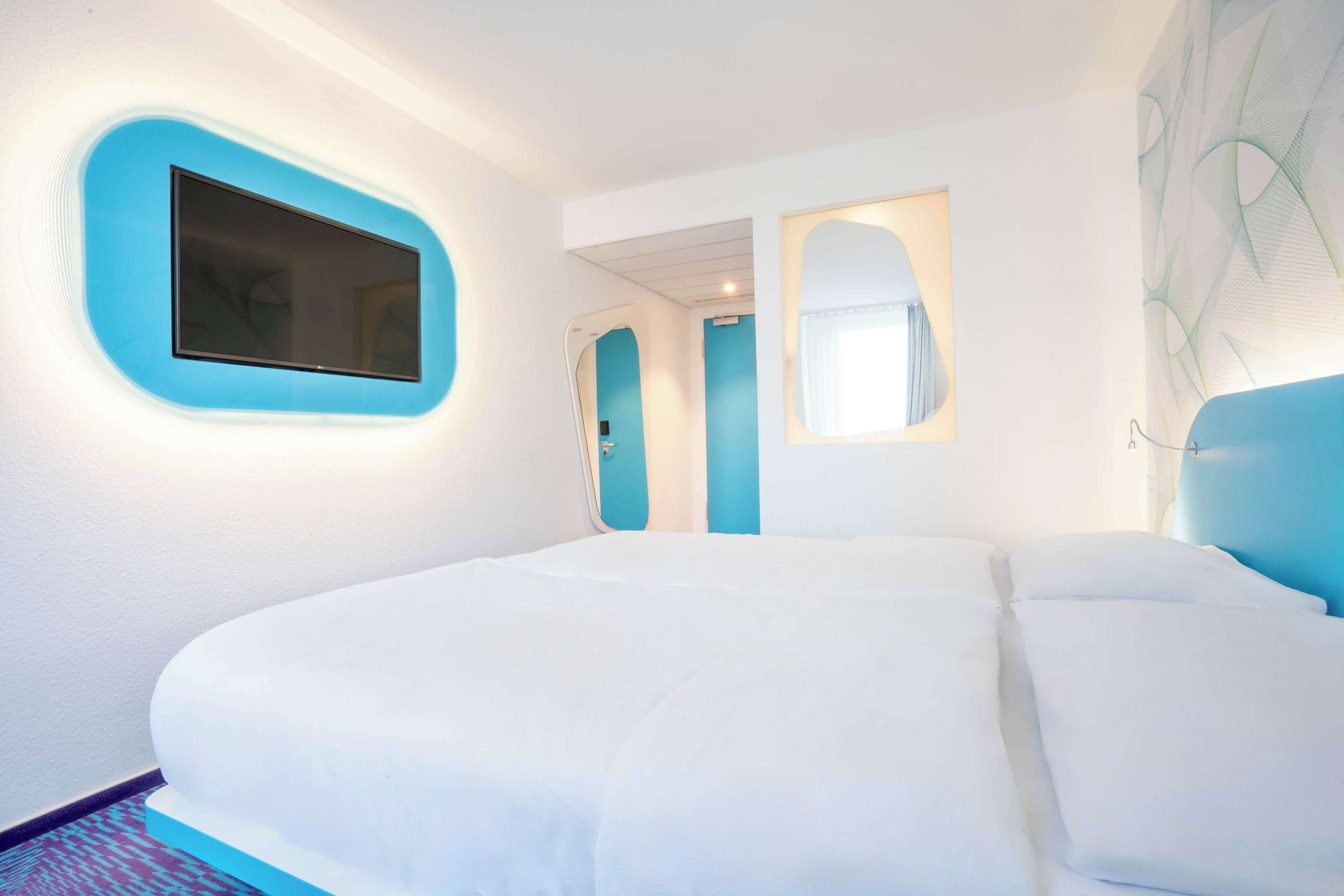A hotel room with a large bed, a TV mounted on the wall, and a mirror.