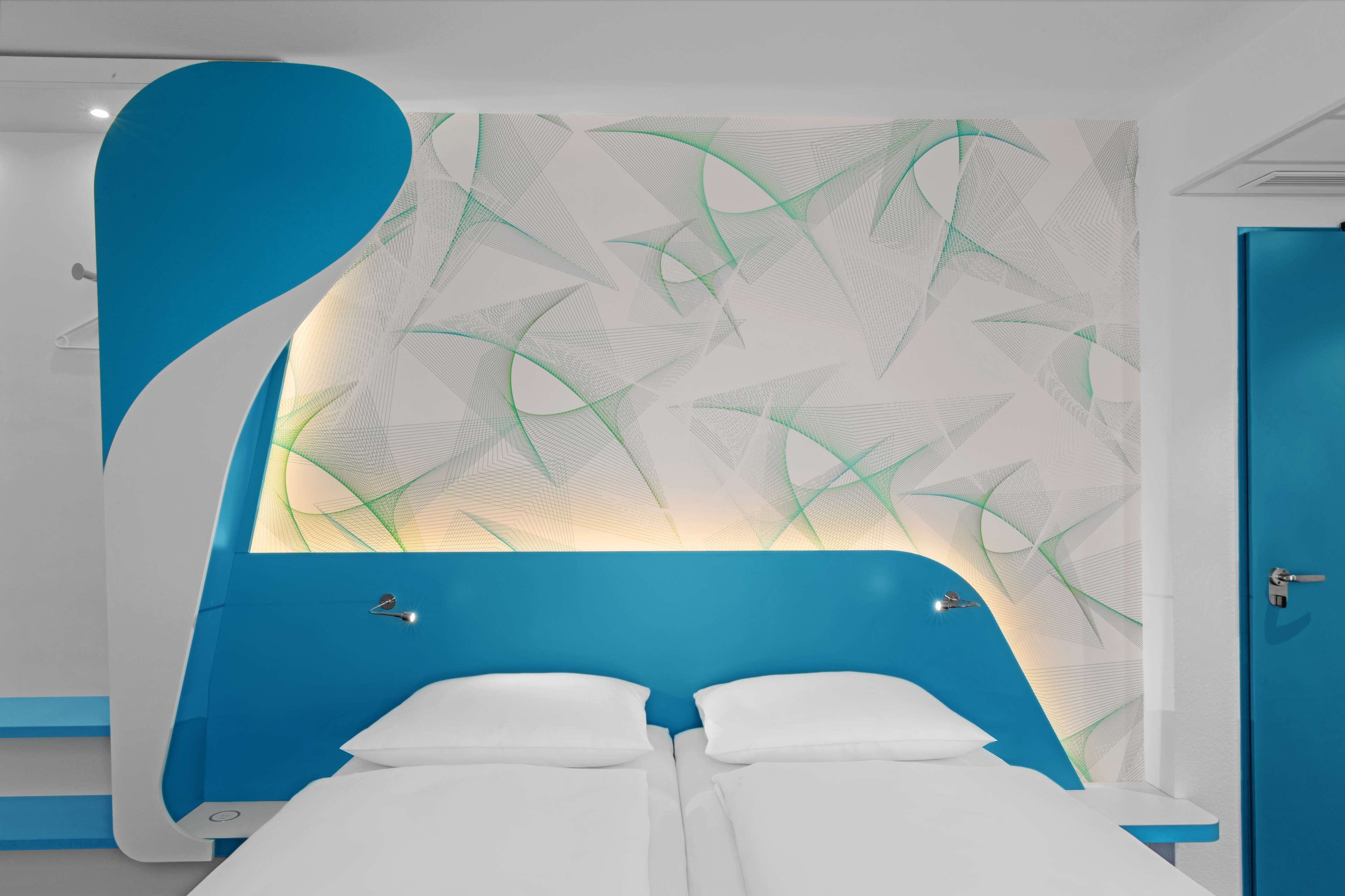 Una habitación de hotel moderna con una pared azul de acento, un patrón geométrico y una cama blanca.