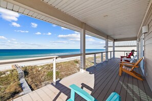 Relax on the deck with a view of the beach, featuring a comfortable seating area with Adirondack chairs and a bench.