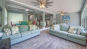 Ein geräumiges Wohnzimmer mit zwei hellblauen Sofas, einem Deckenventilator und einer Küche im Hintergrund.