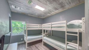 Ein Zimmer mit Etagenbetten, einem Fenster mit Jalousien, einem Schreibtisch und einem Fernseher.