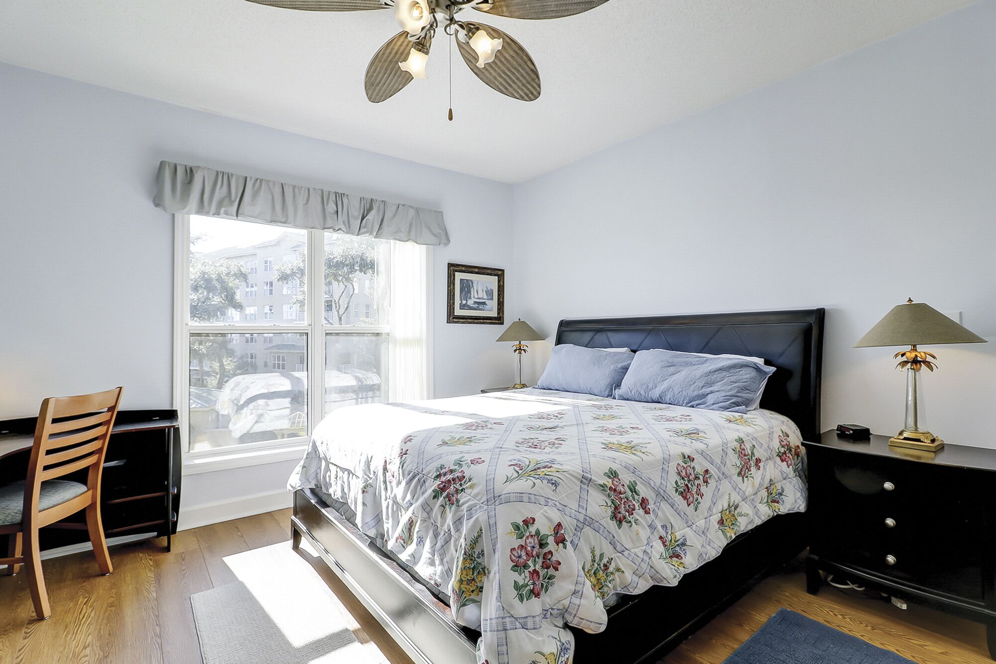 Une chambre à coucher comprenant un lit, un bureau, une chaise, une fenêtre et un ventilateur de plafond.