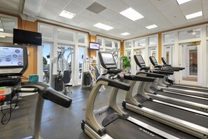 Une salle de sport équipée de tapis de course, d’appareils d’exercice et d’un écran de télévision qui affiche différentes options d’entraînement.