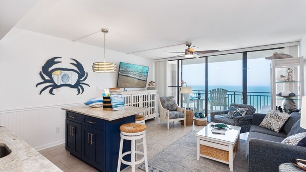 A modern living room with a kitchen area, large windows, and a balcony with a view. - COUPLES ROMANTIC GETAWAY, OCEANFRONT, HIGH-END DECOR, ADJUST. KING, FREE PARKING (Myrtle Beach)