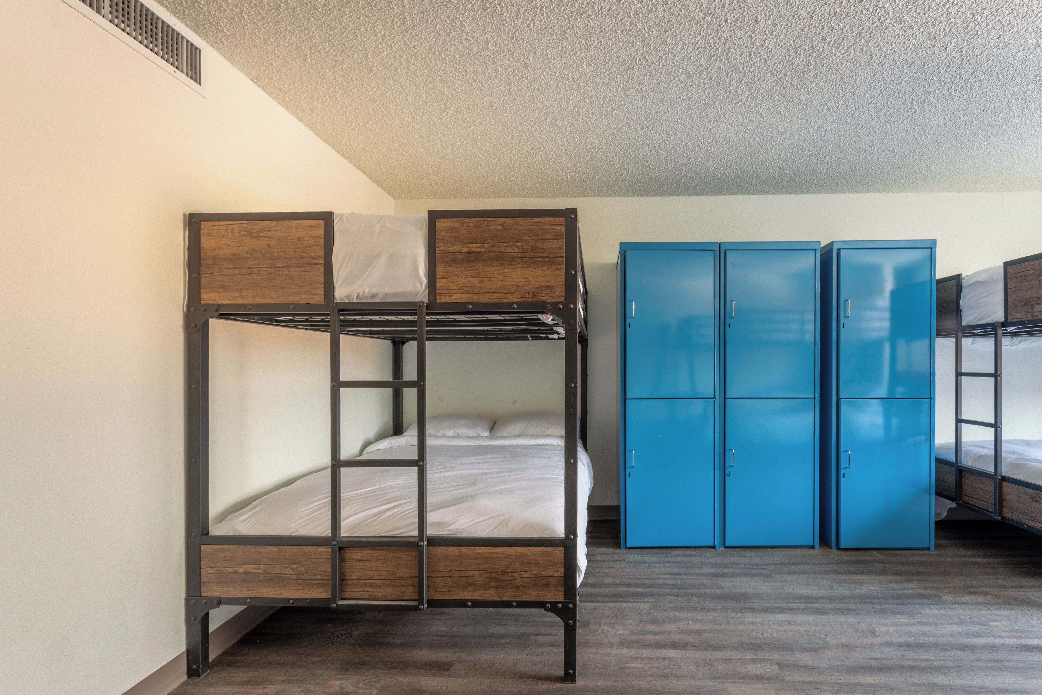 A bunk bed with a wooden headboard, a blue wardrobe, and a mattress on the floor.