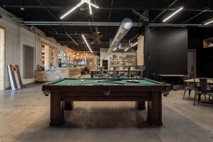 Una sala de billar con mesa de pool, sillas y una zona de bar al fondo.