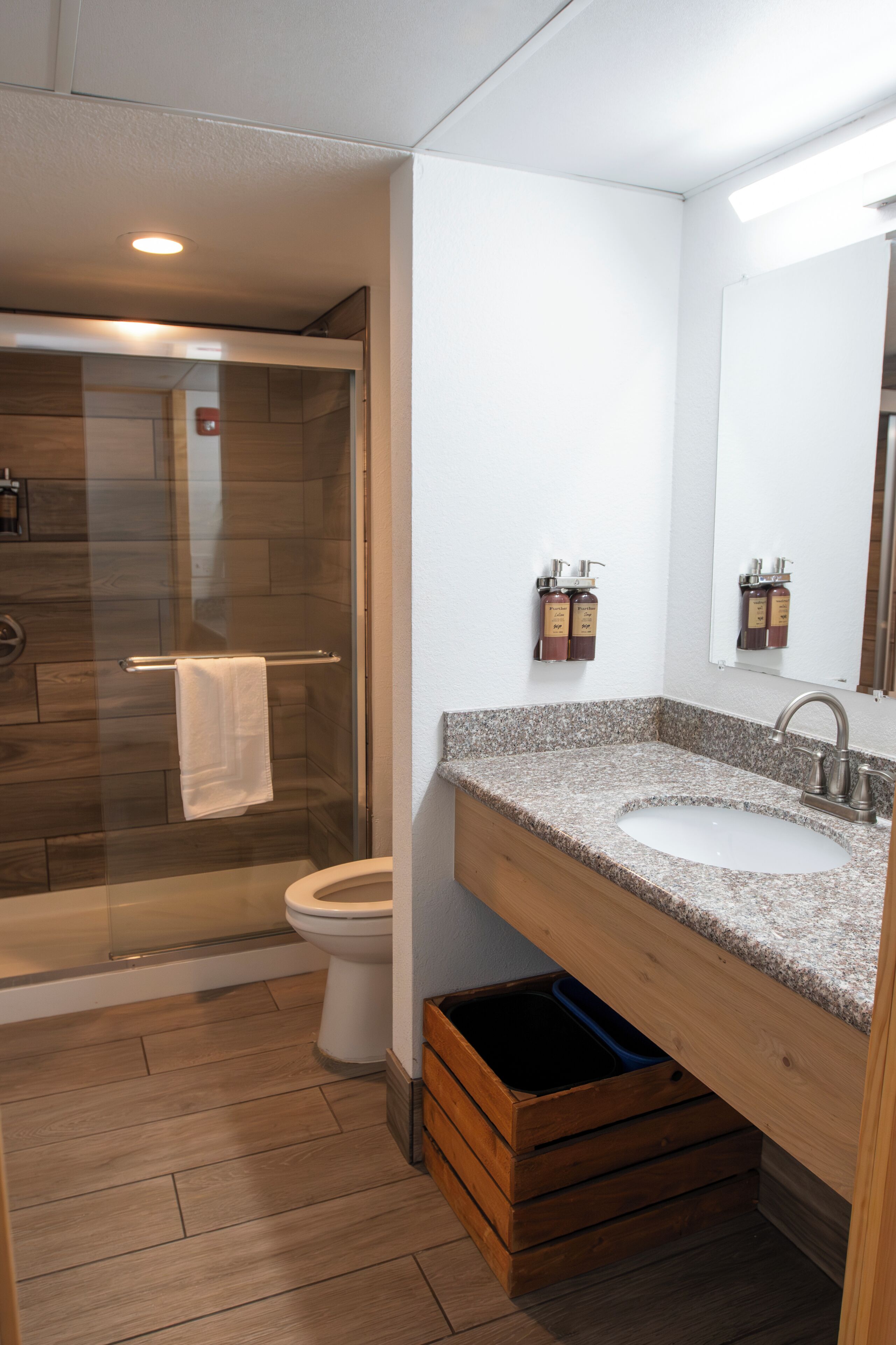 A modern bathroom with a glass shower enclosure, a toilet, a sink with a granite countertop, and a wooden vanity.