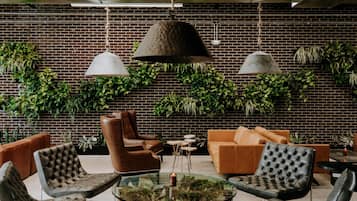 A modern lounge area with leather sofas, a glass coffee table, and hanging plants against a brick wall.