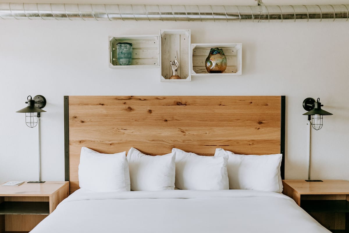 A neatly made bed with white linens, a wooden headboard, and two bedside tables with lamps.