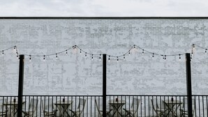 A white brick wall with a weathered texture, a metal fence, and several wooden tables and chairs arranged in front. - SCP WildFree Colorado Springs, Trademark by Wyndham (Colorado Springs)