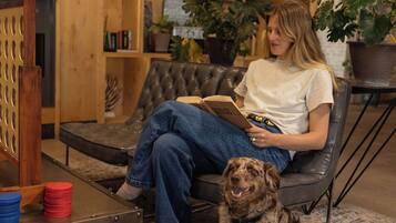 A person sitting on a leather couch reading a book, with a dog beside them.