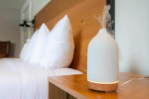 Una habitación con cama, almohadas y una mesita de noche de madera con un dispositivo que emite vapor.