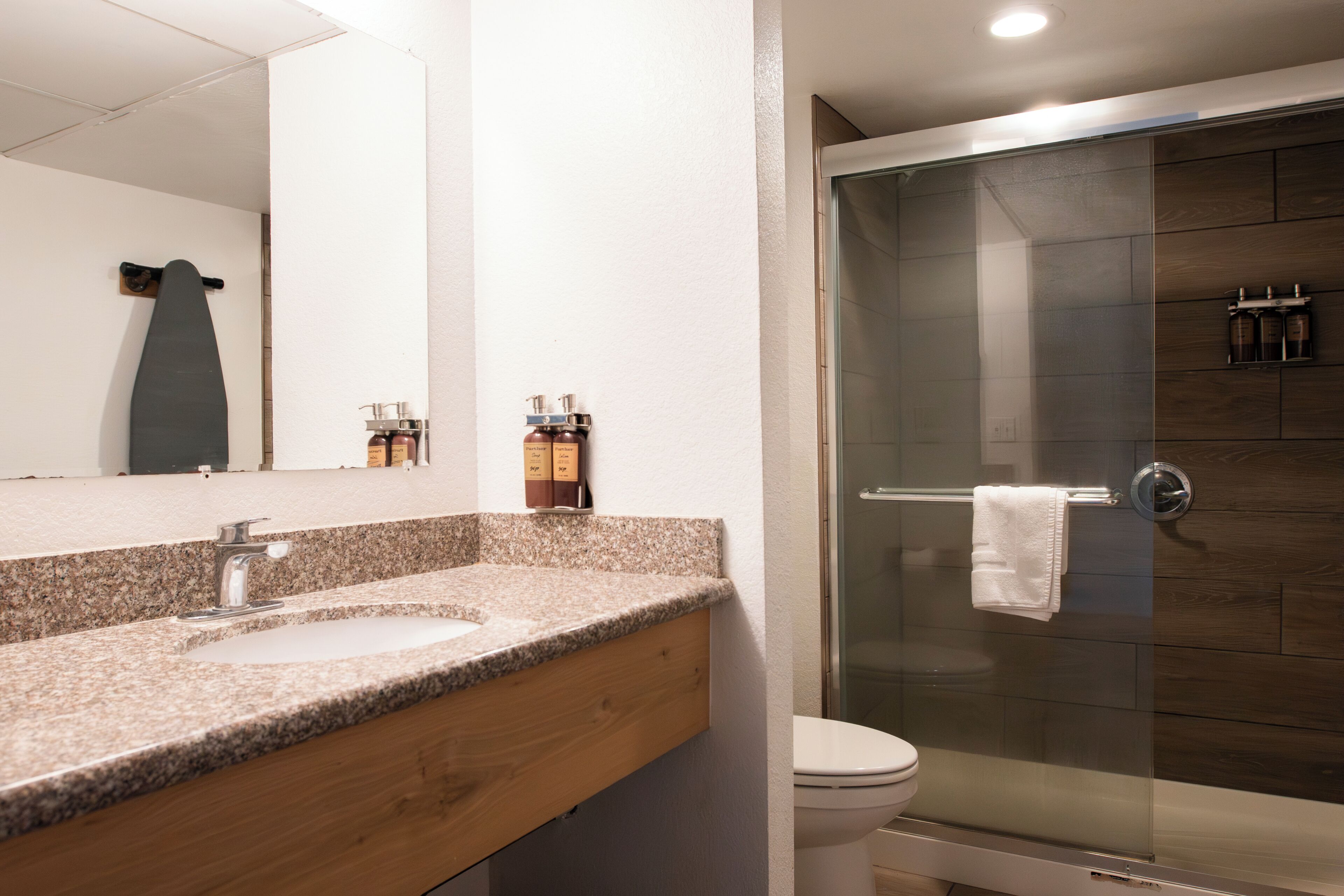 A bathroom with a granite countertop, a mirror, a toilet, and a glass-enclosed shower.