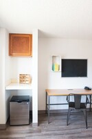 Una habitación pequeña con un armario de madera, una pequeña estantería, una pizarra, un escritorio, una silla y un refrigerador.