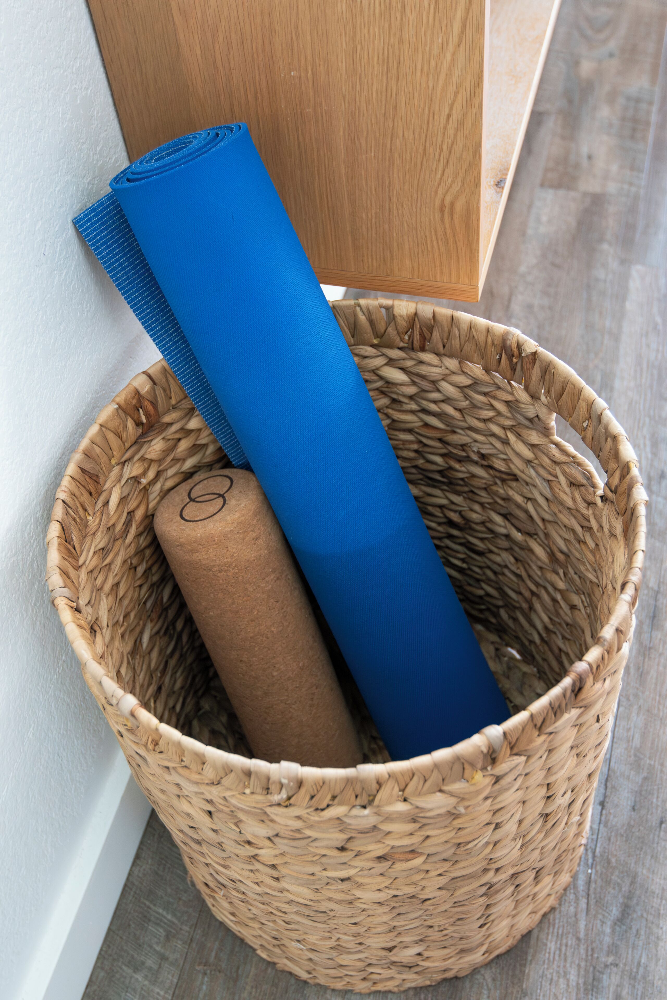 Un panier en osier contenant un tapis de yoga bleu enroulé et un objet cylindrique marron.