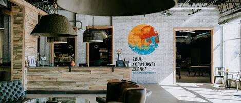 Un interior moderno con paredes de ladrillo visto, un mural grande y una variedad de arreglos de asientos, incluyendo una mesa de vidrio y sillas.