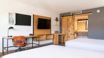 A hotel room with a desk, chair, two beds, a TV, and a sliding door leading to a bathroom.