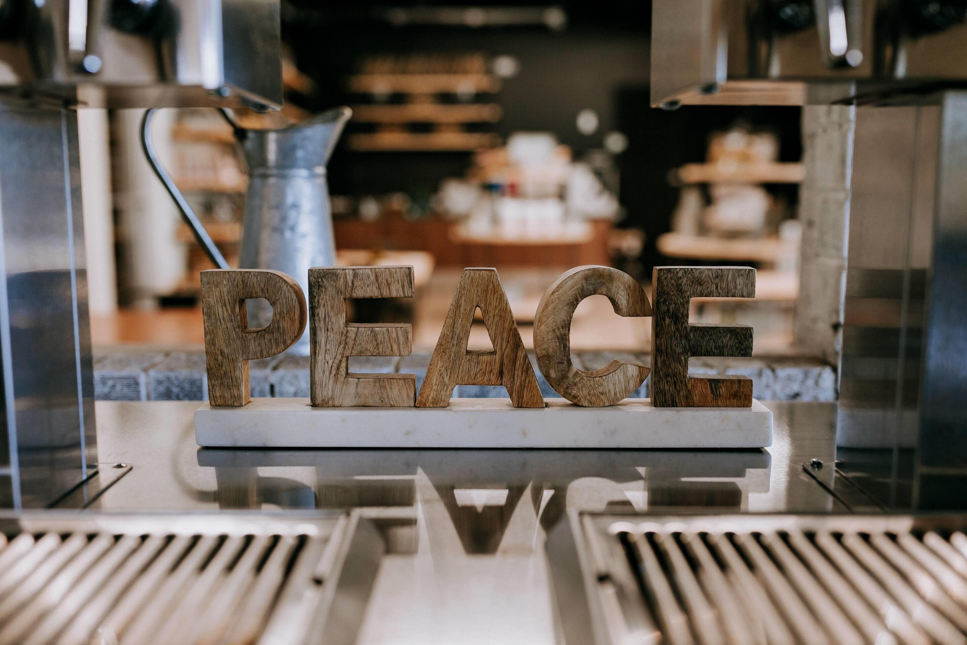 Letras de madera que deletrean 'PEACE' sobre una base blanca, probablemente parte de un adorno o letrero.
